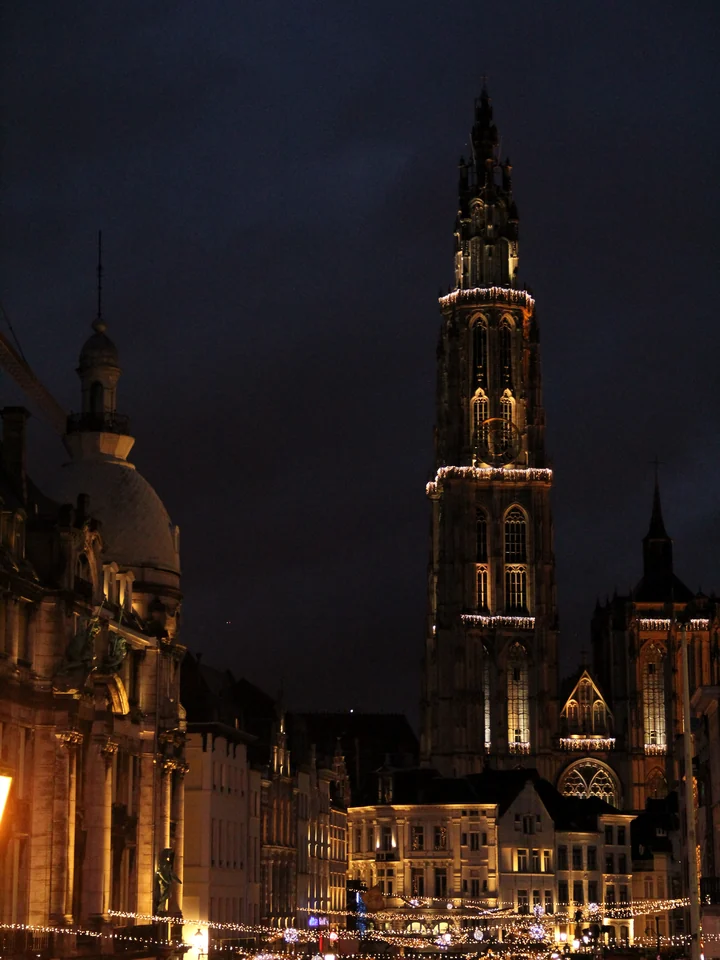 The north tower of the Cathedral of Our Lady in Antwerp at night, lit above the old town and its strings of lights