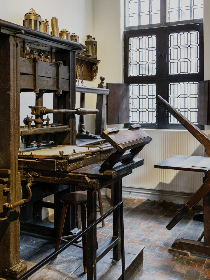 An oak hand press beside a leaded window in the printing room of the Plantin-Moretus house in Antwerp
