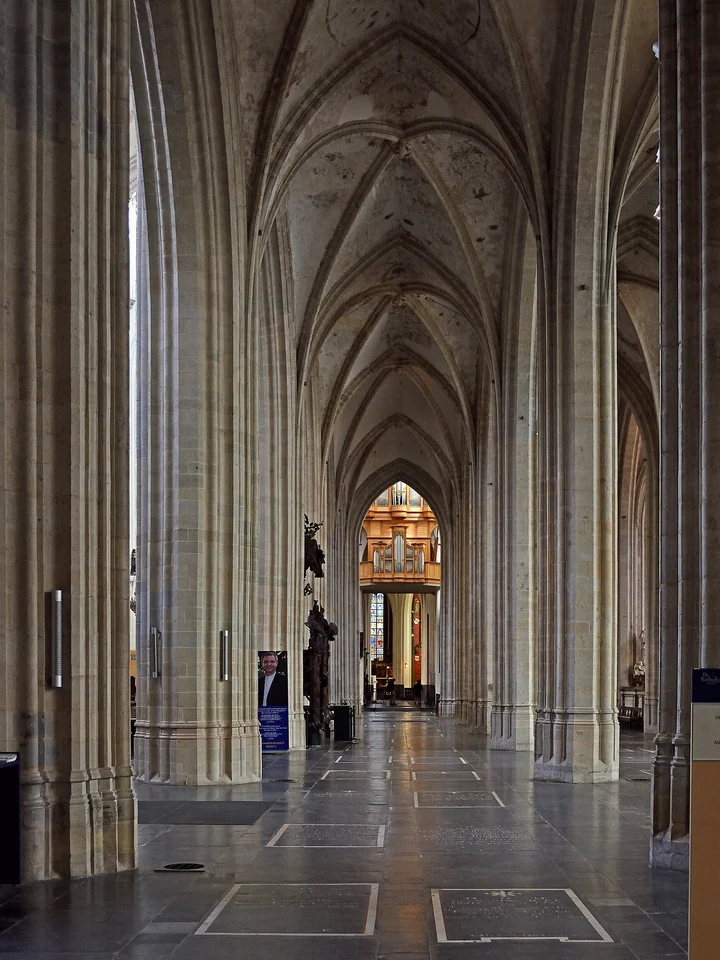 A side aisle of the Cathedral of Our Lady in Antwerp: pale clustered piers rising to ribbed vaults above a dark stone floor with grave slabs