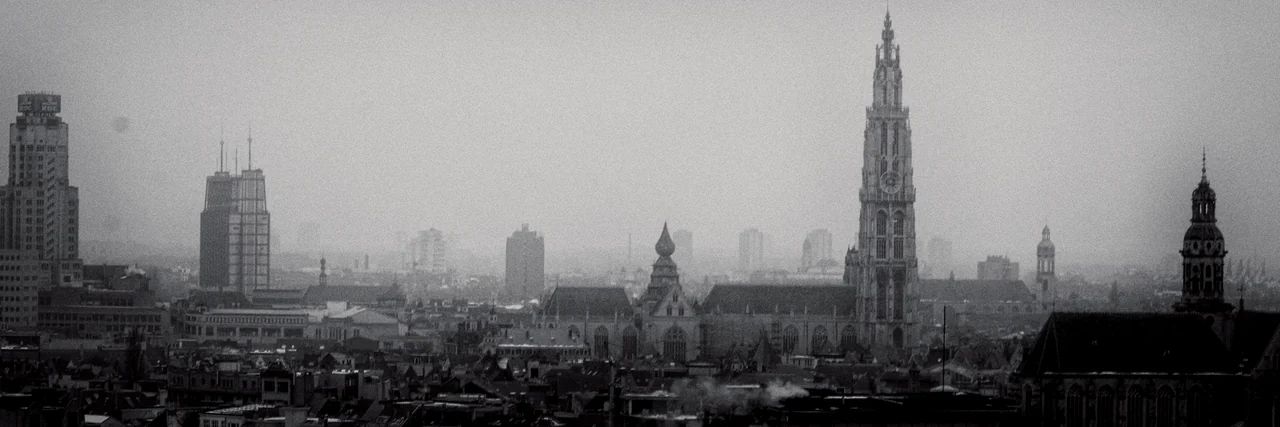 A misty black-and-white view over Antwerp's roofs from the Museum aan de Stroom: the Boerentoren on the left and the cathedral's north tower rising on the right